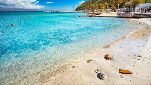 Una playa con agua turquesa cristalina, una orilla arenosa y montañas al fondo.