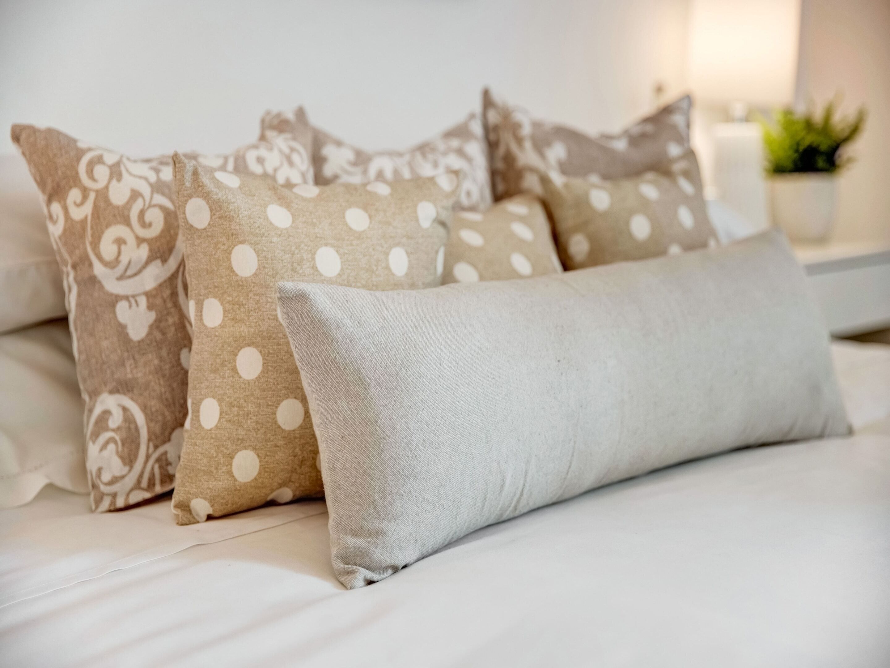 A bed with white bedding, a grey pillow, and patterned pillows.