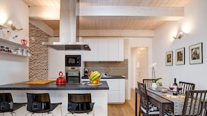 Una cocina moderna con una isla central, taburetes de bar, una mesa de comedor con sillas y un horno a la vista.