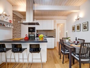 A modern kitchen with a central island, bar stools, a dining table with chairs, and a visible oven. - Civico36 Feels Like Home (Cagliari)