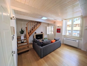 Un salon avec un canapé gris, un escalier en bois, une télévision et une grande fenêtre.
