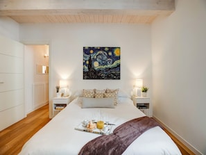 Une chambre à coucher avec un lit, des tables de chevet, une commode, un tableau et un plateau de petit-déjeuner.
