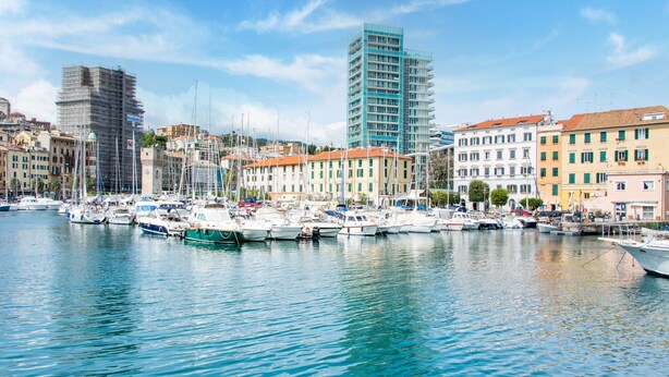 Un port de plaisance où sont amarrés des bateaux, entouré de bâtiments aux couleurs vives et d’une grande structure moderne.