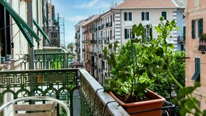Un balcon orné d’un pot de fleurs, donnant sur une rue bordée de bâtiments historiques et offrant une vue sur un ciel dégagé.
