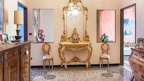 Une pièce comprenant un grand miroir décoratif, deux chaises, une commode en bois et une table sur laquelle se trouve une horloge.