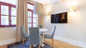 A modern room with a dining table, four chairs, a TV mounted on the wall, and a window with curtains. - Oporto Home Wine Cellars - Estúdio c/ Terraço 1ºT (Vila Nova de Gaia)