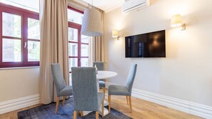 Una habitación moderna con una mesa de comedor, cuatro sillas, un televisor montado en la pared y un ventanal con cortinas.