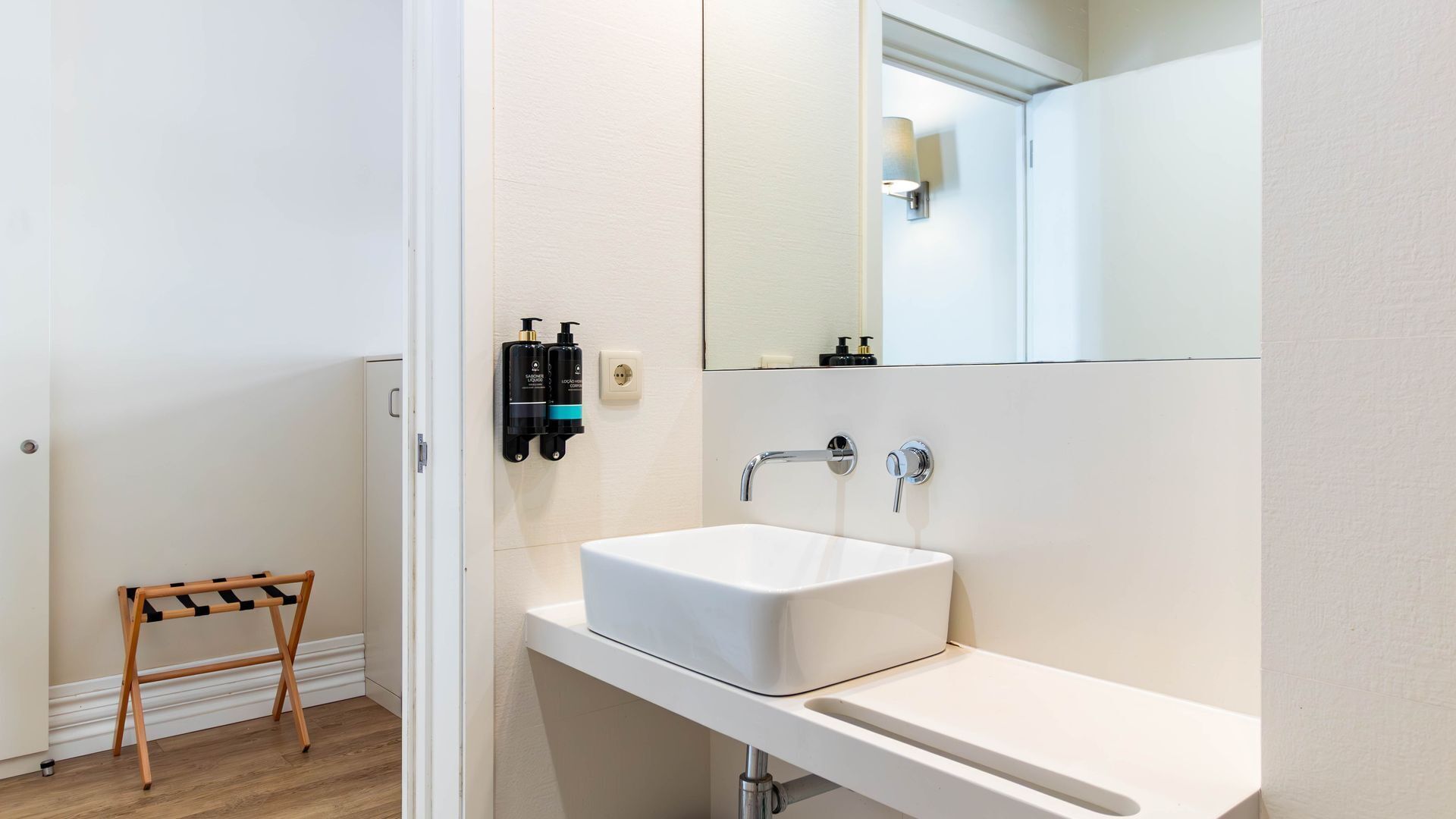 Un baño con un lavabo blanco, un espejo y un taburete de madera.