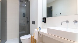 Un baño moderno con ducha envuelta en vidrio, un lavamanos blanco y un espejo grande.
