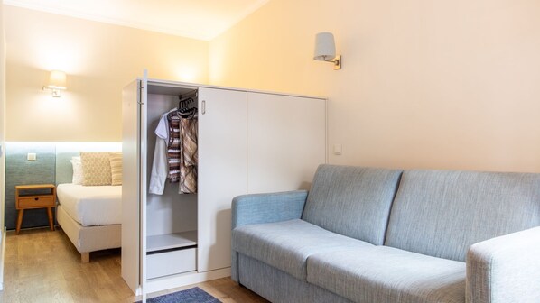 Un dormitorio con una cama, un armario, un sofá gris y una mesita de noche.