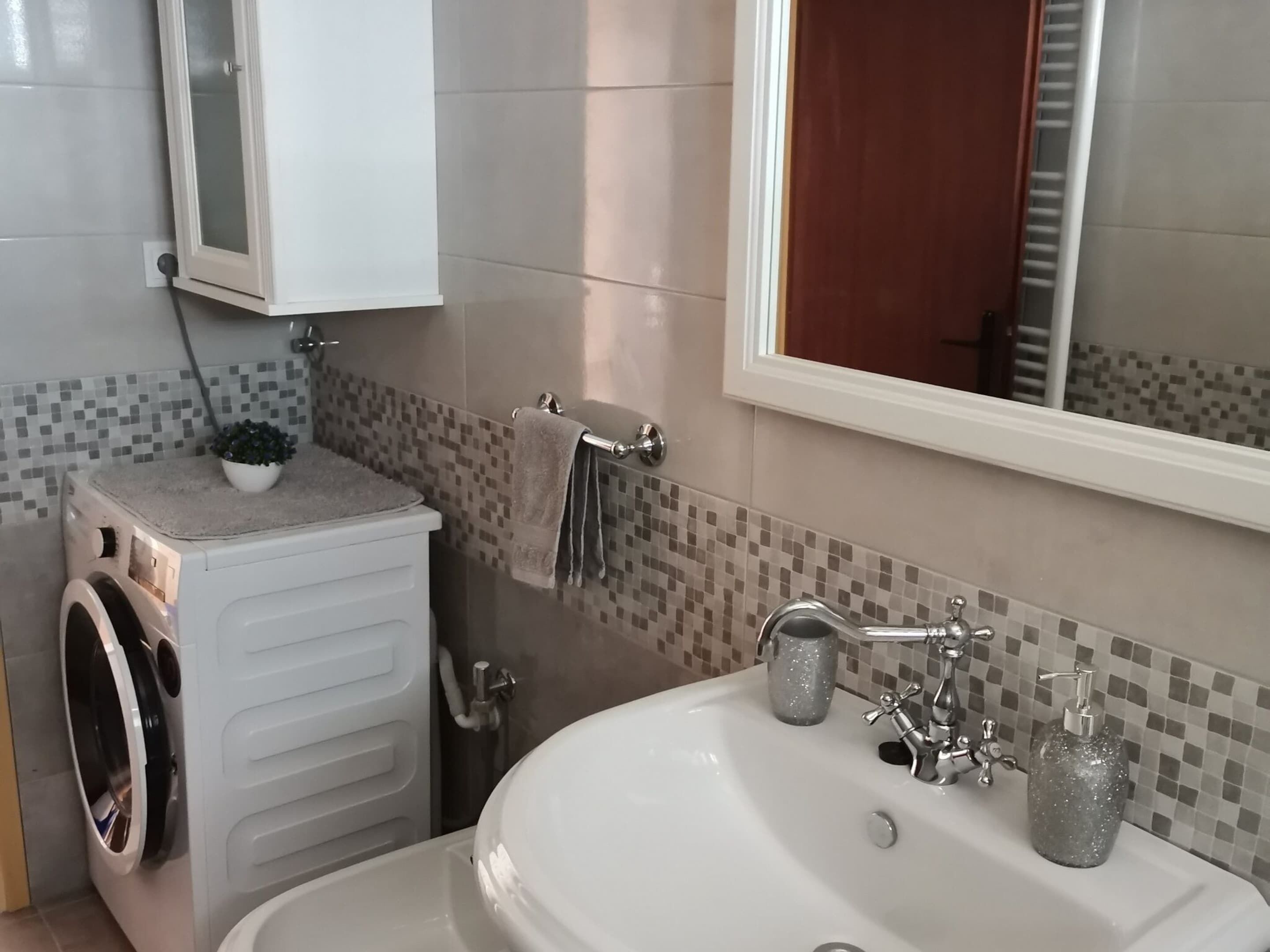A bathroom with a washing machine, a sink, and a mirror.