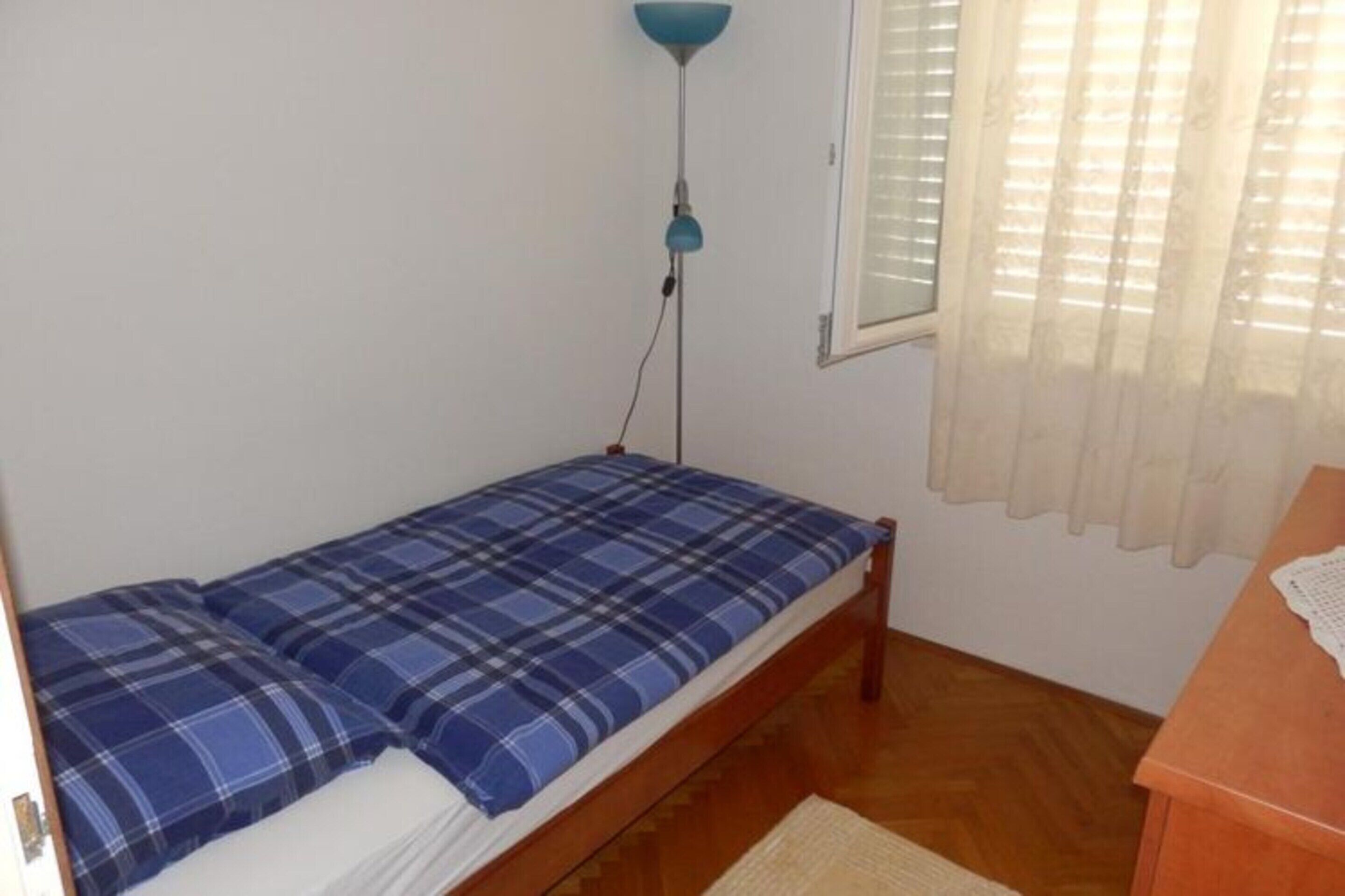 A small room with a single bed, a wooden desk, a lamp, and a window with curtains.