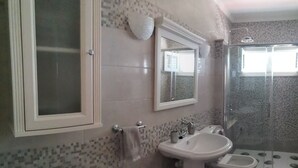 Un baño con pared de azulejos, lavamanos, espejo, ducha y bañera.
