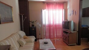 Una sala de estar con un sofá, una mesa de centro, un televisor sobre un mueble y una puerta que da a otra habitación.