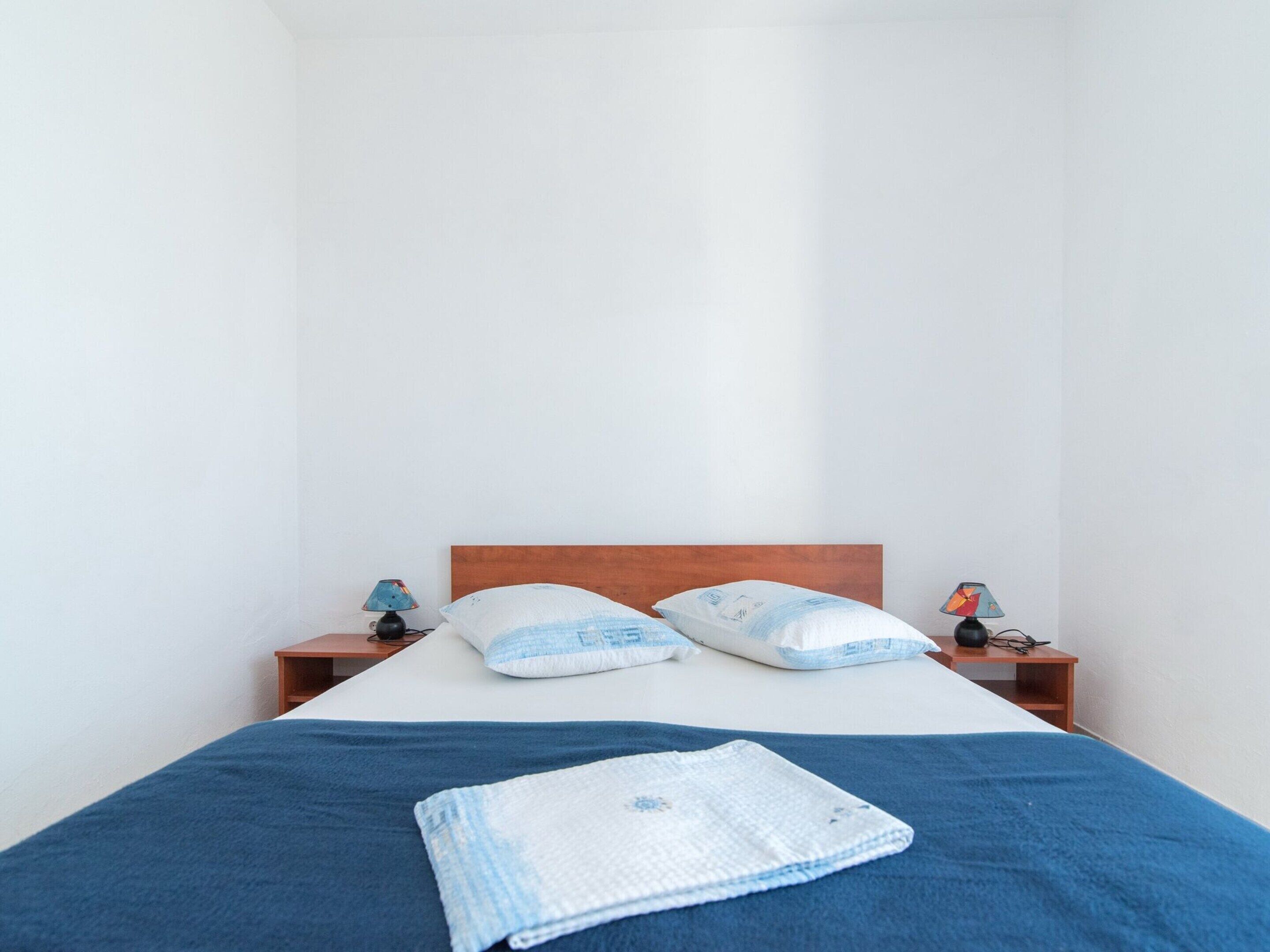 Uma cama de casal com cabeceira de madeira, duas mesas de cabeceira com abajures e um cobertor azul na cama.