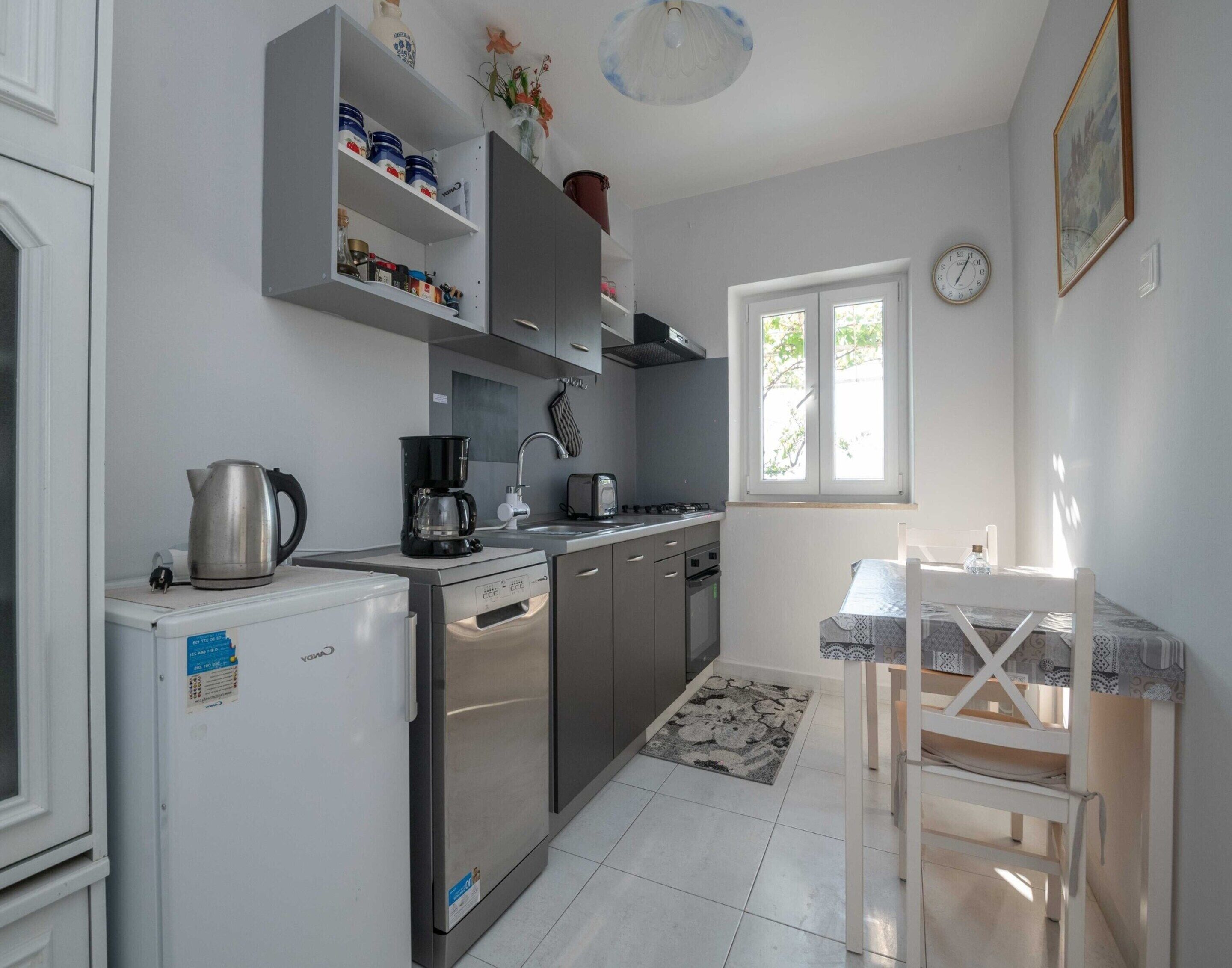 A compact kitchen with a refrigerator, stove, and sink. There is a window providing natural light and a small dining table with chairs.