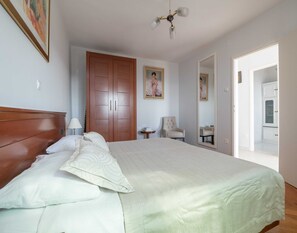 Un dormitorio con una cama grande, un armario de madera, una mesita, una silla y un espejo.