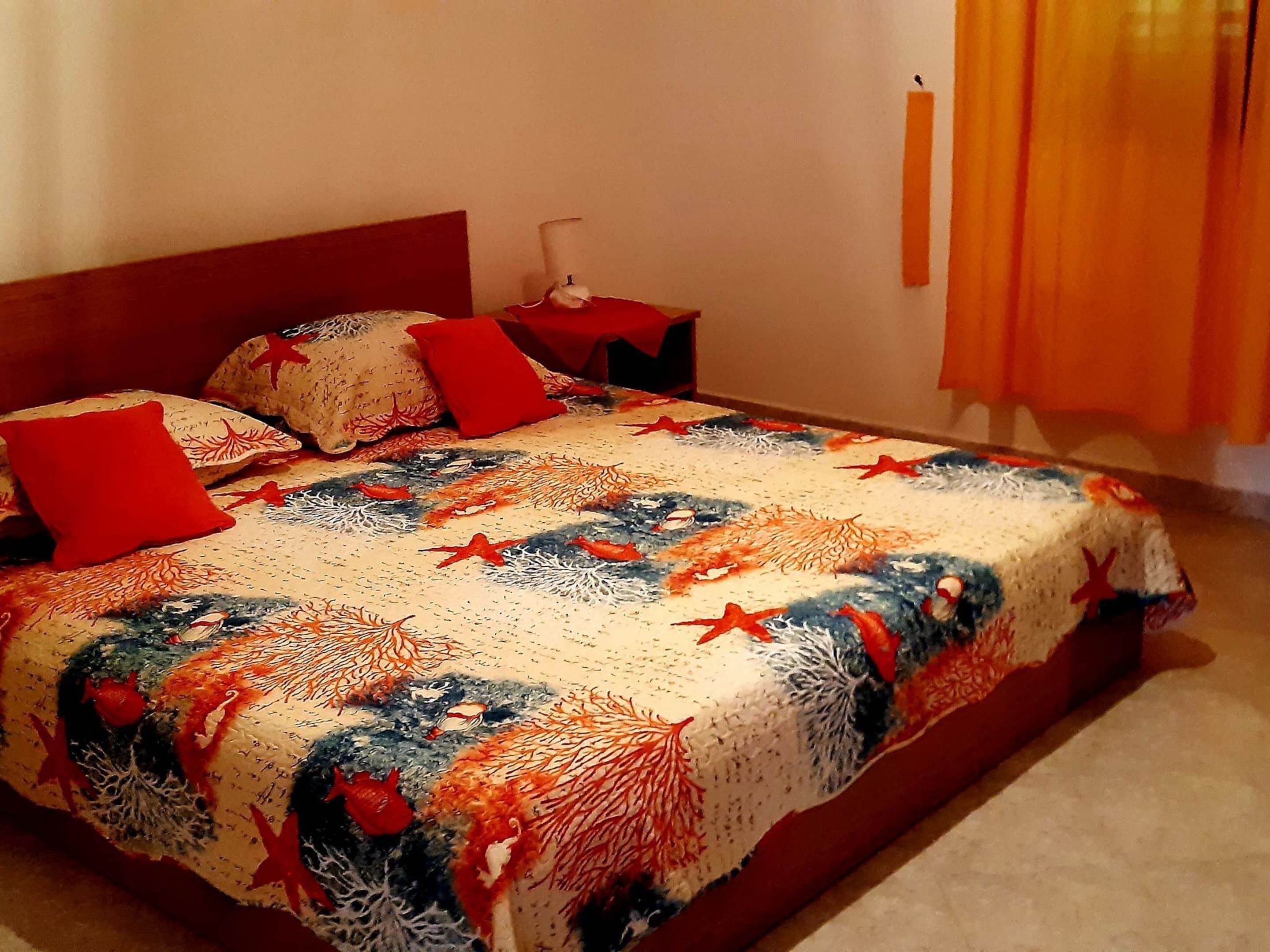 A bed with a patterned bedspread, red pillows, and a nightstand with a lamp.