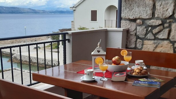 A wooden table with breakfast items, a view of the sea, and a stone wall. - Apartments Cumbelic - One Bedroom Apartment With Balcony and Sea View A1 (Mljet)