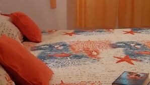Un dormitorio con una cama, almohadas anaranjadas, una colcha estampada y un libro sobre la cama.
