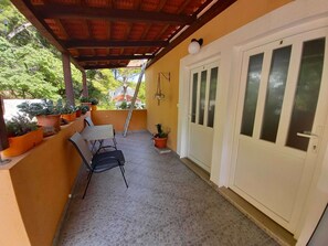 Eine überdachte Terrasse mit Tisch, Stühlen, Topfpflanzen und einer Tür mit Milchglasfenstern.
