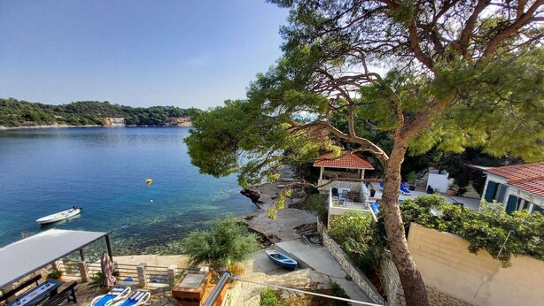 A coastal property with a stone patio, lounge chairs, a small boat, and a view of the sea. - Apartments Vinko Mljet- One-bedroom Apartment With Terrace (Mljet)