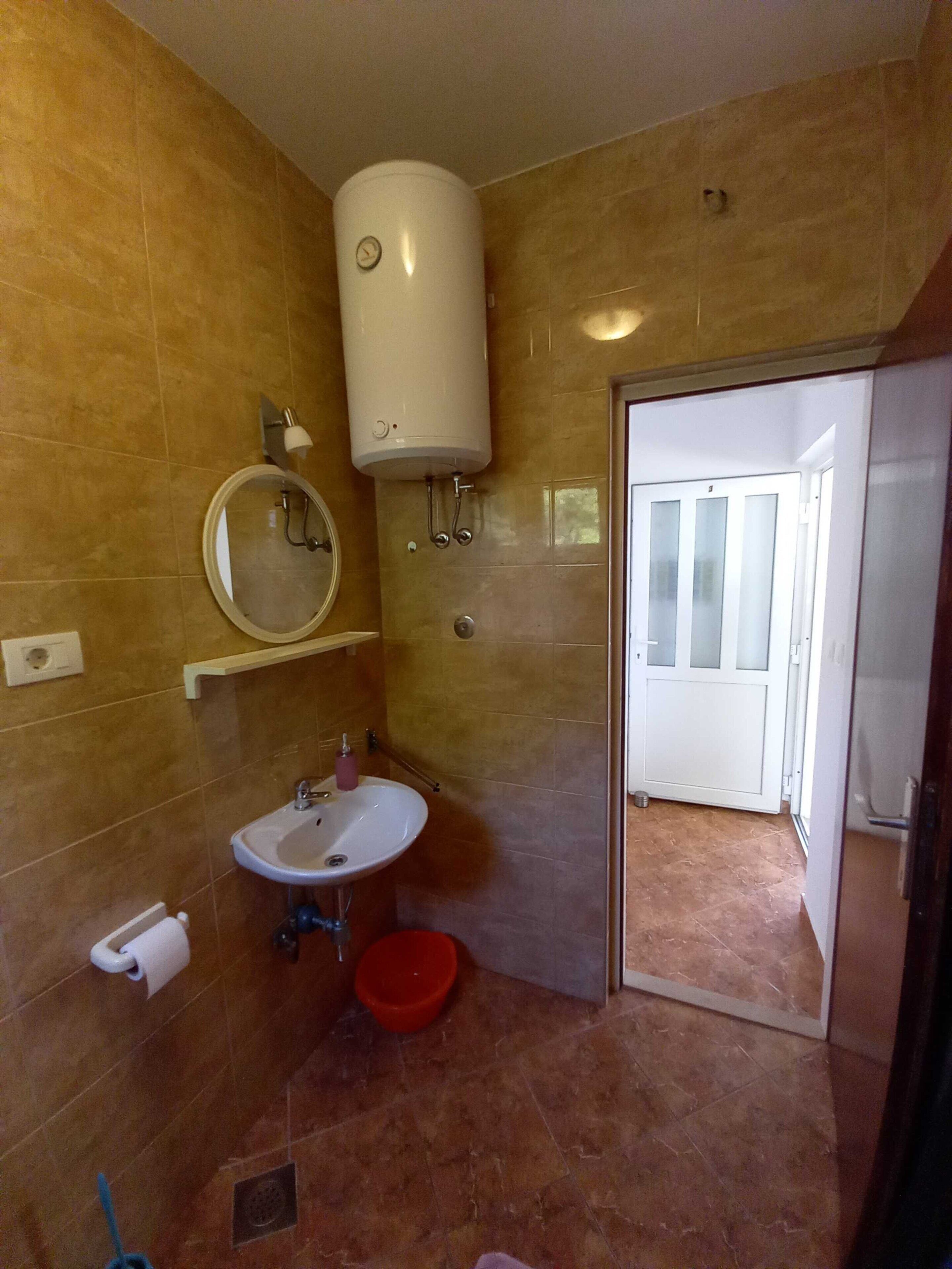 A bathroom with a sink, mirror, toilet, and a white water heater on the wall.