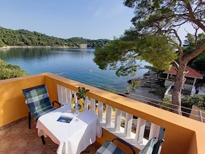 Ein Balkon mit Tisch und Stühlen mit Blick auf einen See, umgeben von viel Grün und einem kleinen Gebäude mit rotem Dach.