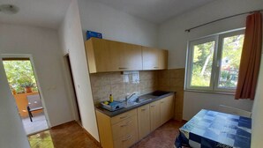 A compact kitchen with a sink, countertop, and cabinets. There is a window with curtains and a view of greenery outside. - Apartments Vinko Mljet- One-bedroom Apartment With Terrace (Mljet)