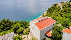 A coastal building with a red roof, surrounded by greenery and overlooking a calm sea. - Villa Kosa - Standard Double Room With Balcony and Sea View (Brela)