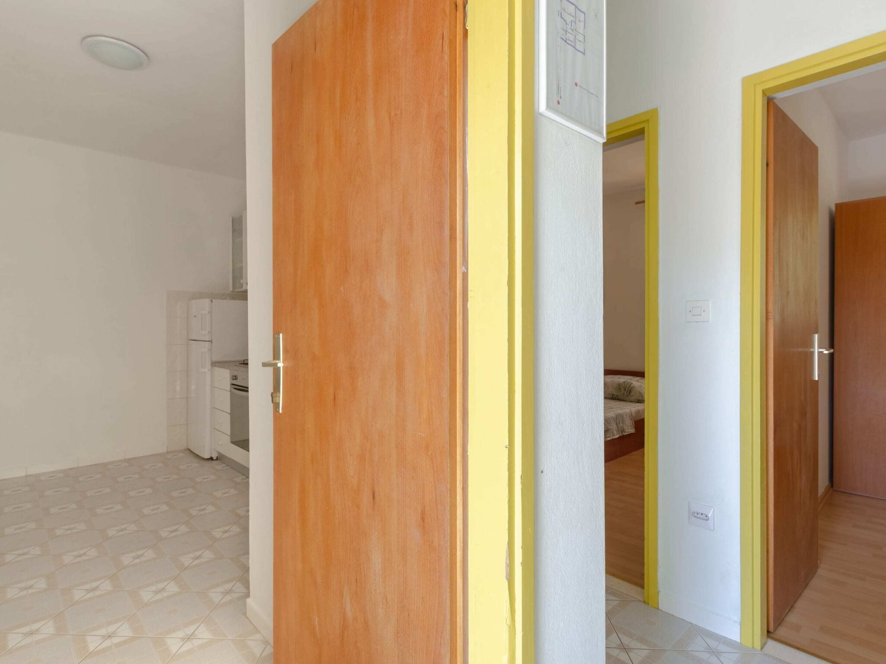 A room with a wooden door, a white wall with a door frame, and a tiled floor.