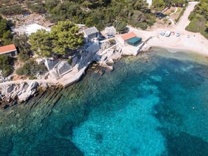 An aerial view of a coastal property with a stone building, a sandy beach, and clear turquoise waters. - Seafront Apartments Olivera-two Bedroom Apartment With Patio (Blato)