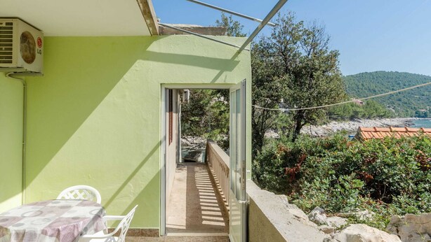 Ein Balkon mit Tisch und Stühlen, Blick auf das Meer und eine grüne Wand.