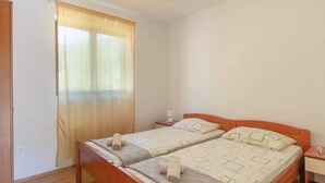 Ein Doppelbett mit zwei Kissen und einer Decke, ein Nachttisch aus Holz, ein Fenster mit Vorhängen und eine Tür.