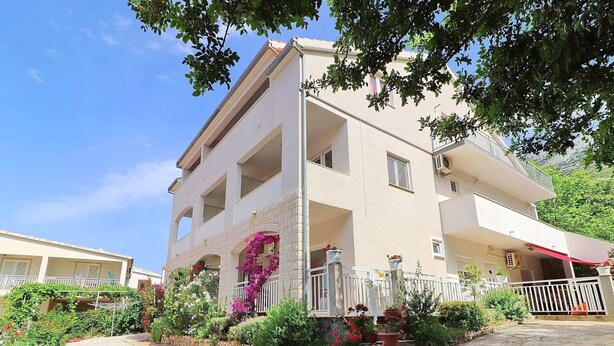 A multi-story building with balconies, a stone wall, and potted plants. - Apartments Marko Peljesac - Standard One Bedroom Apartment With Balcony (Orebic)
