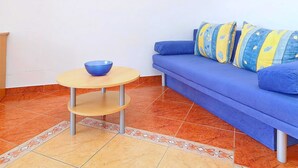 A room with a blue sofa, a small round table with a bowl, a framed picture on the wall, and patterned floor tiles. - Apartments Marko Peljesac - Standard One Bedroom Apartment With Balcony (Orebic)