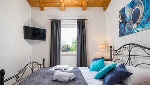 Une chambre à coucher avec un lit, une télévision, une fenêtre avec des rideaux et un tableau au mur.