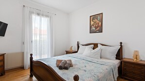 A bedroom with a wooden bed, a bedside table, a nightstand, a painting on the wall, and a window with curtains. - Stylish Villa in Buje With Outdoor Kitchen (Buje)