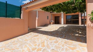 A covered outdoor area with stone flooring, a pergola with climbing plants, and a building entrance with a large window. - Stylish Villa in Buje With Outdoor Kitchen (Buje)