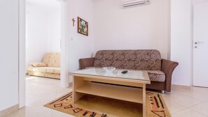 A living room with a sofa, a glass-top coffee table, a patterned cushion, a rug, and an air conditioning unit on the wall. - Apartment in Medulin With Balconies (Medulin)