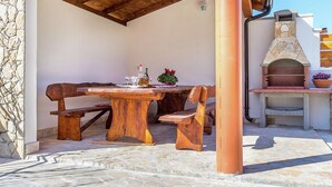 Une terrasse extérieure avec une table et des bancs en bois, un sol en pierre et un four en pierre.