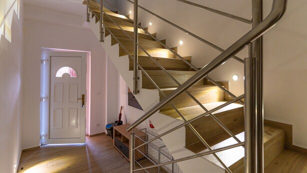 Eine moderne Treppe mit Holzboden und Metallgeländern, die zu einer Zwischenebene mit einer Bank und einer Tür führt.
