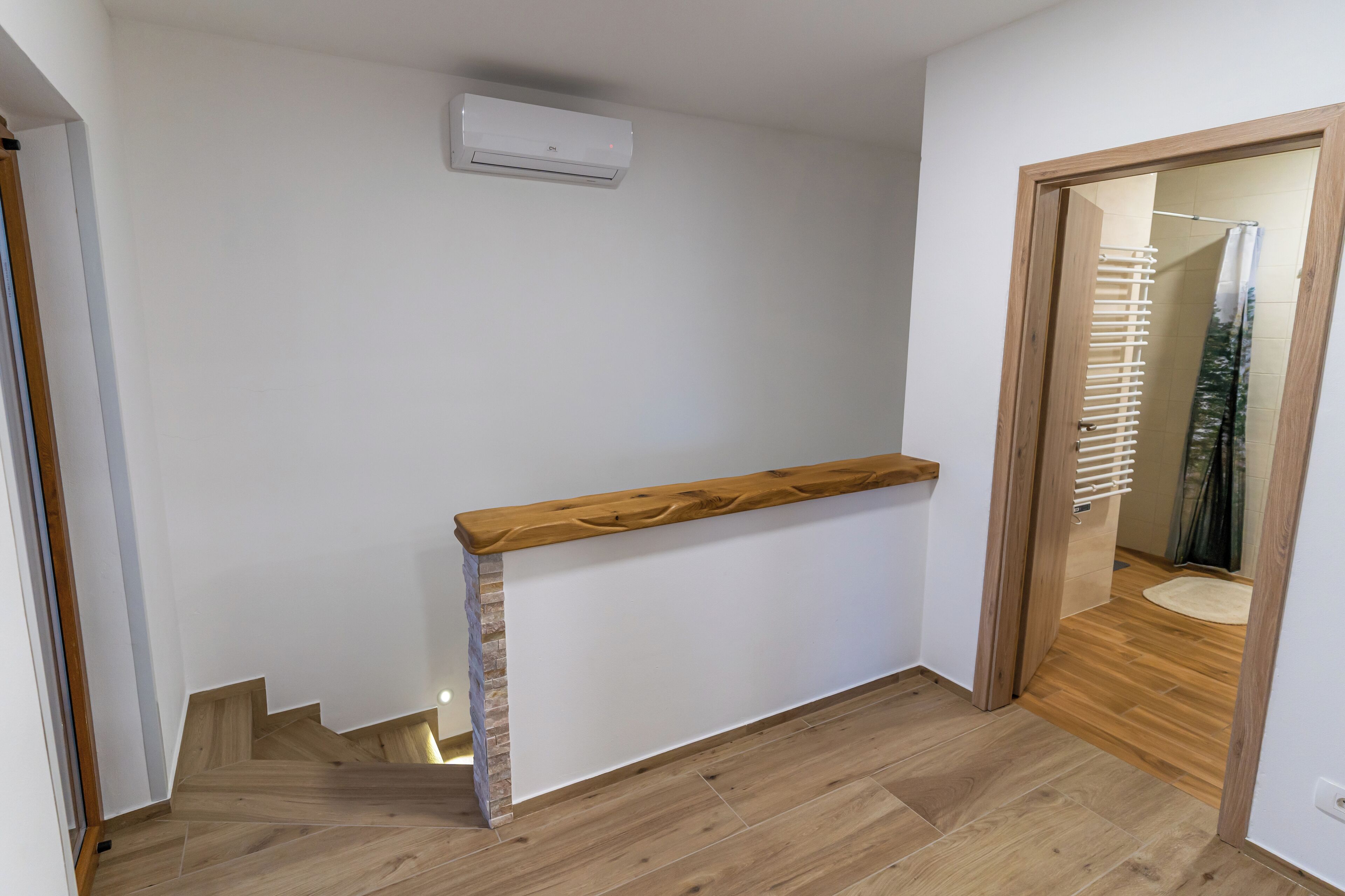 A staircase with wooden steps and a wooden handrail, leading to a room with white walls and a wooden floor.