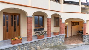 Ein zweistöckiges Gebäude mit Natursteinfundament, Holztüren und einer überdachten Terrasse mit Sitzgelegenheiten.