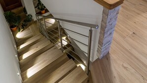 Eine Holztreppe mit Metallgeländer, die zu einem Raum mit einer Waschmaschine und einem Bett mit blauer Decke führt.