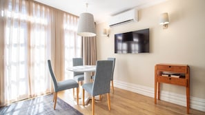 A dining area with a round table, four chairs, a TV mounted on the wall, and a wooden side table.