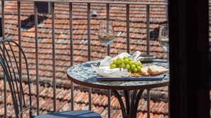 Une table ronde recouverte d’une nappe blanche, une assiette de raisins verts, un morceau de fromage et deux verres de vin blanc.