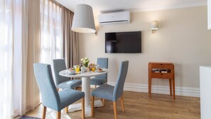 Un coin repas comprenant une table ronde, quatre chaises, un téléviseur fixé au mur et un appareil de climatisation.