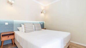 Une chambre d’hôtel comprenant un lit, deux tables de chevet et deux lampes fixées au mur.