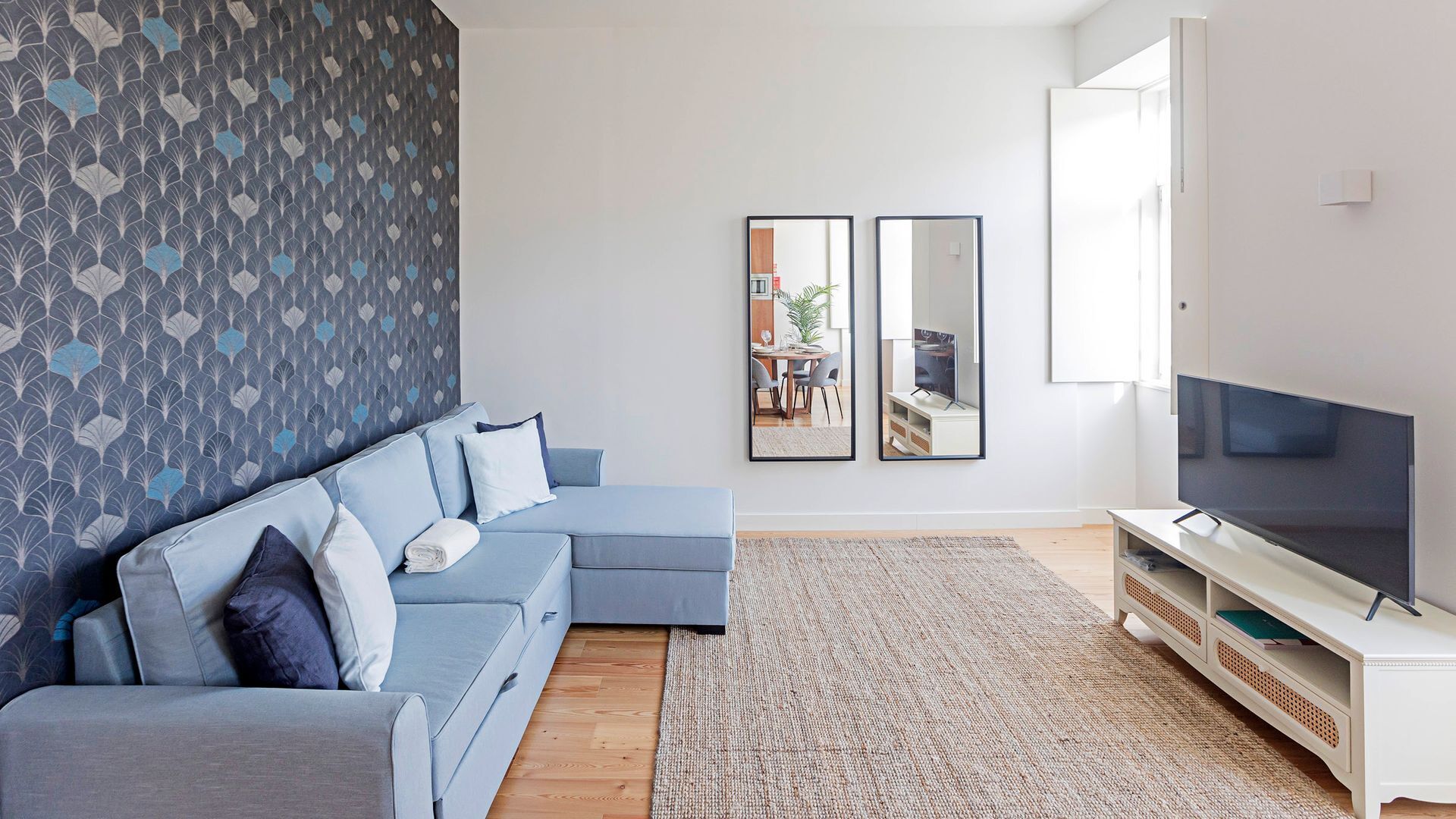 Un salon moderne avec un canapé d’angle, un téléviseur à écran plat et deux tableaux encadrés accrochés au mur.